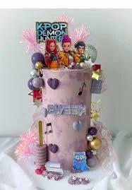 Tall purple and pink textured cake with K-Pop Demon Hunter character printouts, music notes, and purple heart accents.