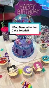 Purple K-Pop Demon Hunter themed cake with blue icing ruffles, pink and silver disco balls, and character cupcakes.