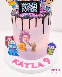 Pink 1-tier K-Pop Demon Hunters themed cake with black chocolate drip, colorful sprinkles, and character printouts.