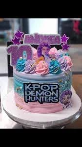 K-Pop Demon Hunters themed cake with pink and blue gradient icing, purple character printouts, and colorful icing swirls.