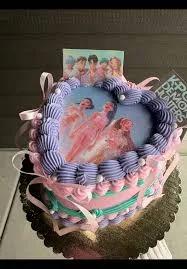 Heart-shaped K-pop themed cake with pink and purple ruffled icing, featuring printed character toppers and a central photo.