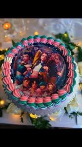 Round K-pop themed birthday cake with a large circular character printout and pink and teal piped icing borders.