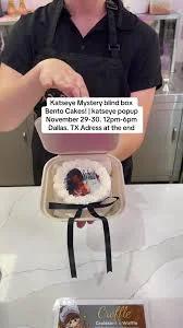 White bento cake with a printed photo of a person and a black ribbon bow in a takeout container.