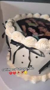 White vintage-style cake with black bows, black polka dots, and a printed photo of the K-pop group Katseye on top.
