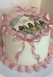 Pink and white Katseye K-pop themed cake with edible photo print, pink ribbon bows, and piped icing borders.