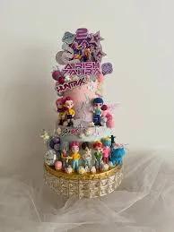 Three-tier purple and pink K-pop themed cake with multiple character figurines and printed toppers.