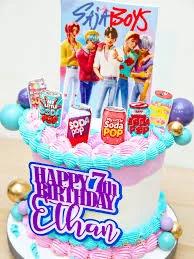 Colorful K-pop themed birthday cake for Ethan with printed boy band toppers, soda can cutouts, and pink and blue icing swirls.