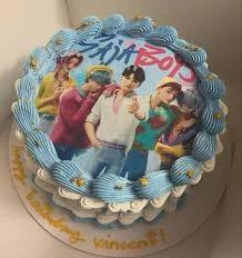 Blue and white K-pop themed birthday cake with a large printed photo of a boy band and blue icing swirls.