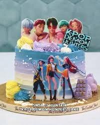 K-Pop Demon Hunters themed cake with blue and purple gradient icing, character printouts, and colorful meringue kisses.