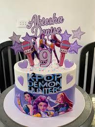 White and purple Kpop Demon Hunters themed cake with character printouts and purple stars.