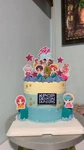 K-Pop Demon Hunters themed birthday cake with blue and yellow gradient icing, character printouts, and star toppers.