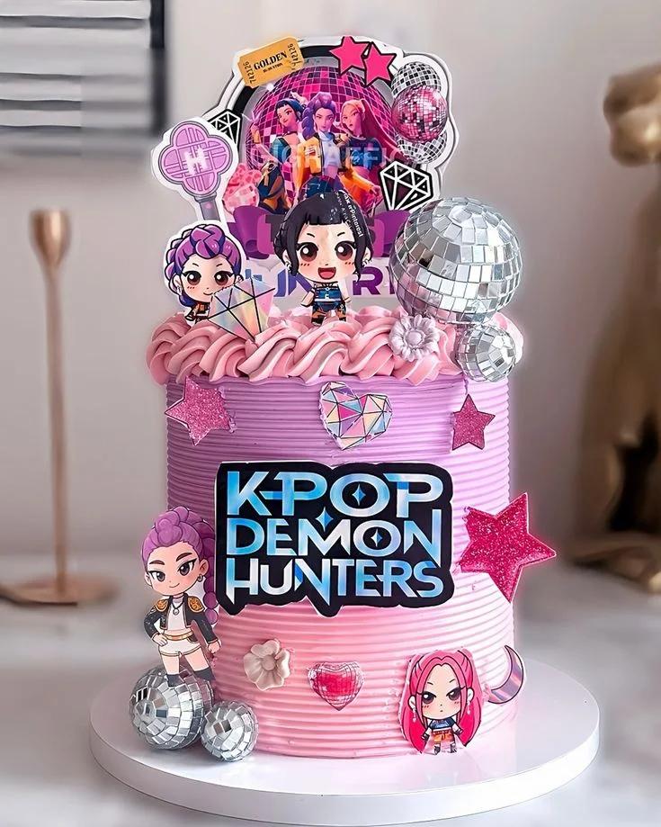 Pink and purple K-Pop Demon Hunters themed cake with disco balls, character printouts, and glittery stars.