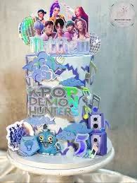 Tall 1-tier K-Pop Demon Hunters themed cake in light blue and purple with character printouts, speakers, and musical notes.