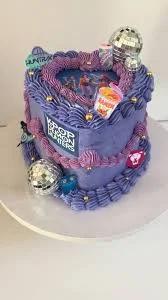 Purple heart-shaped K-pop themed cake with disco balls, ramen cup printout, and intricate purple icing borders.