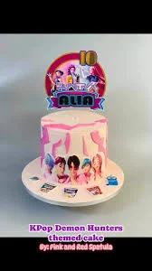 KPop Demon Hunters themed cake with pink and white textured icing and character printouts