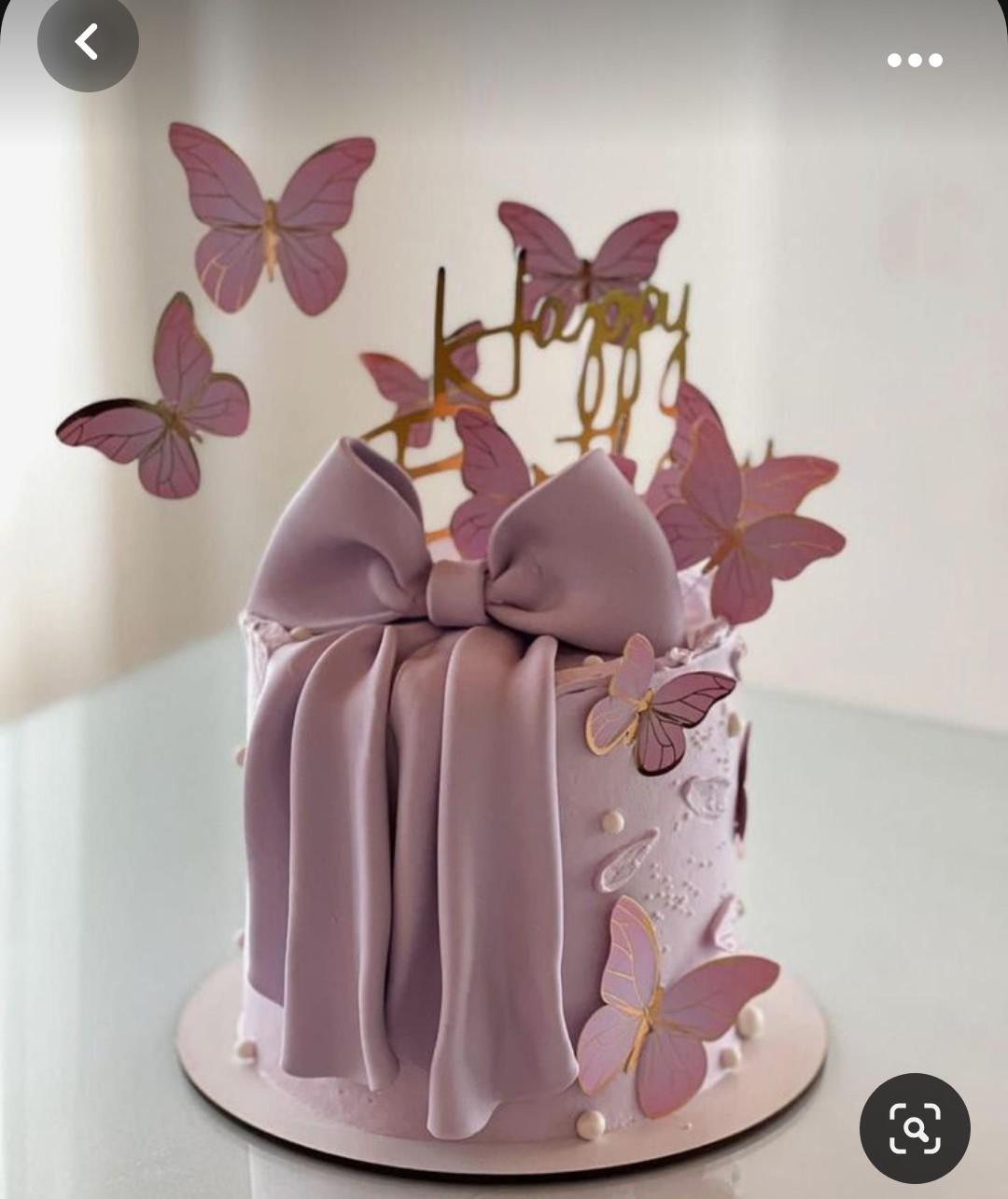 Lavender purple cake with a large fondant bow, gold Happy Birthday topper, and purple butterfly decorations.