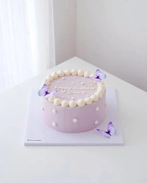 Minimalist lavender purple cake with white icing dollops, edible butterflies, and white pearls.
