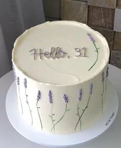 Minimalist white 1-tier cake with purple lavender floral icing decorations and silver Hello 31 message on top.