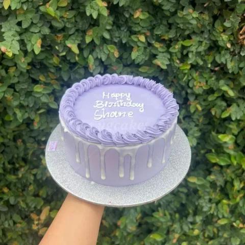 Minimalist lavender purple cake with white icing drip and piped border featuring a Happy Birthday Shane message.