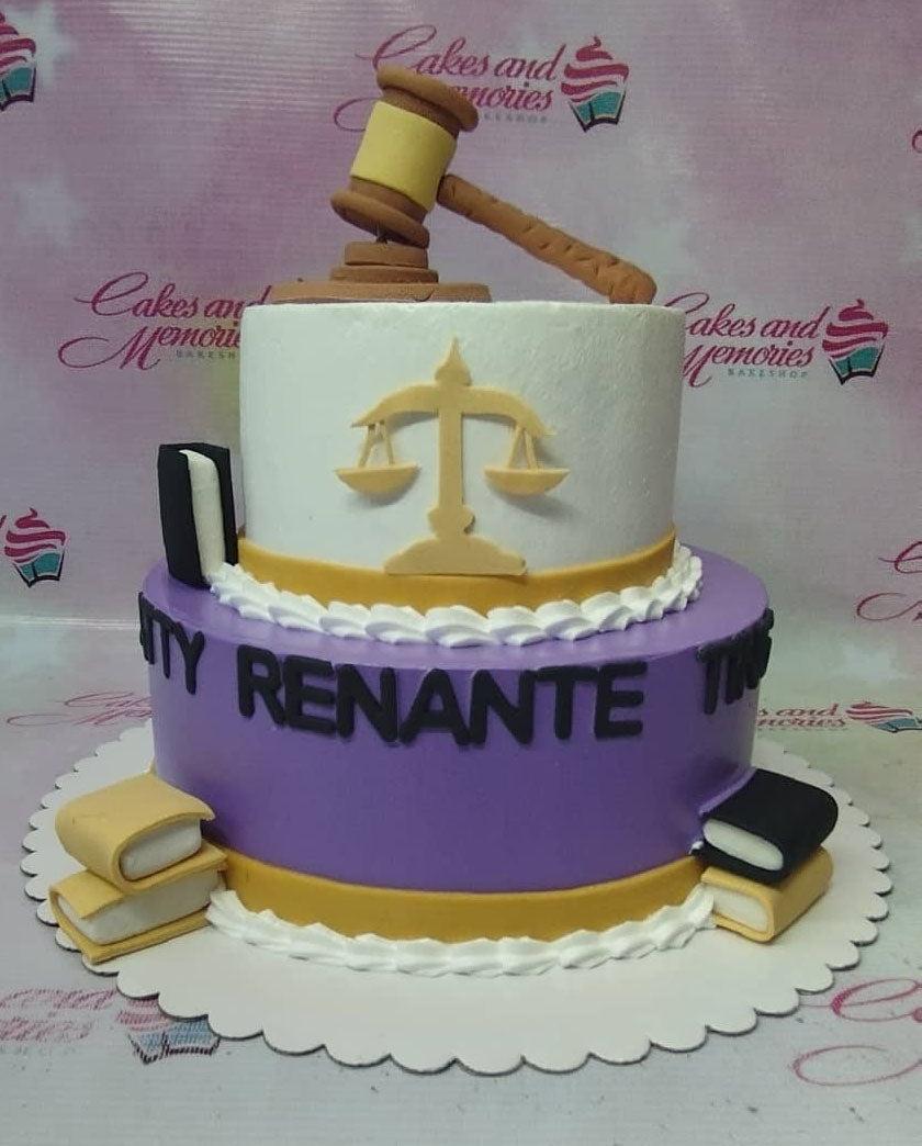 Two-tier law-themed cake in purple and white with a gavel topper, scales of justice, and fondant law books.
