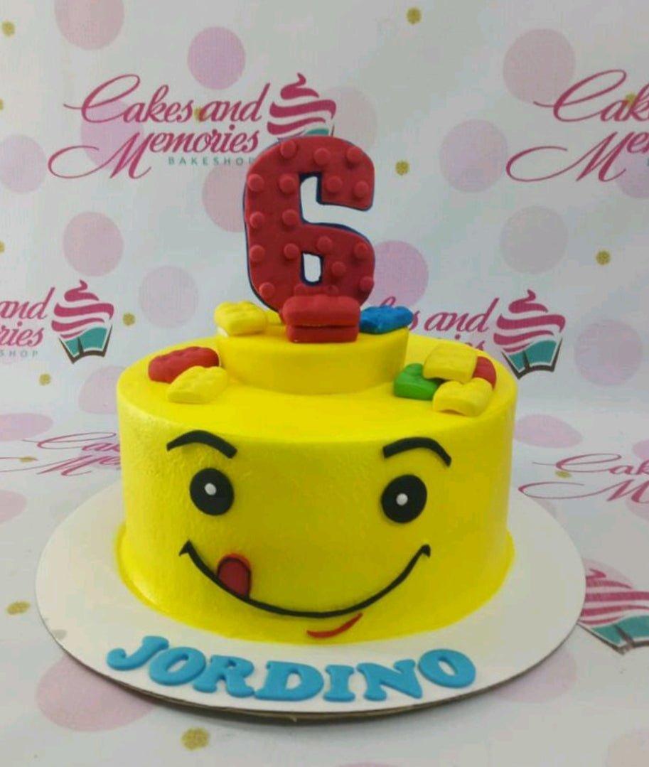 Yellow Lego head cake with a large red number 6 topper and colorful fondant building blocks on top.