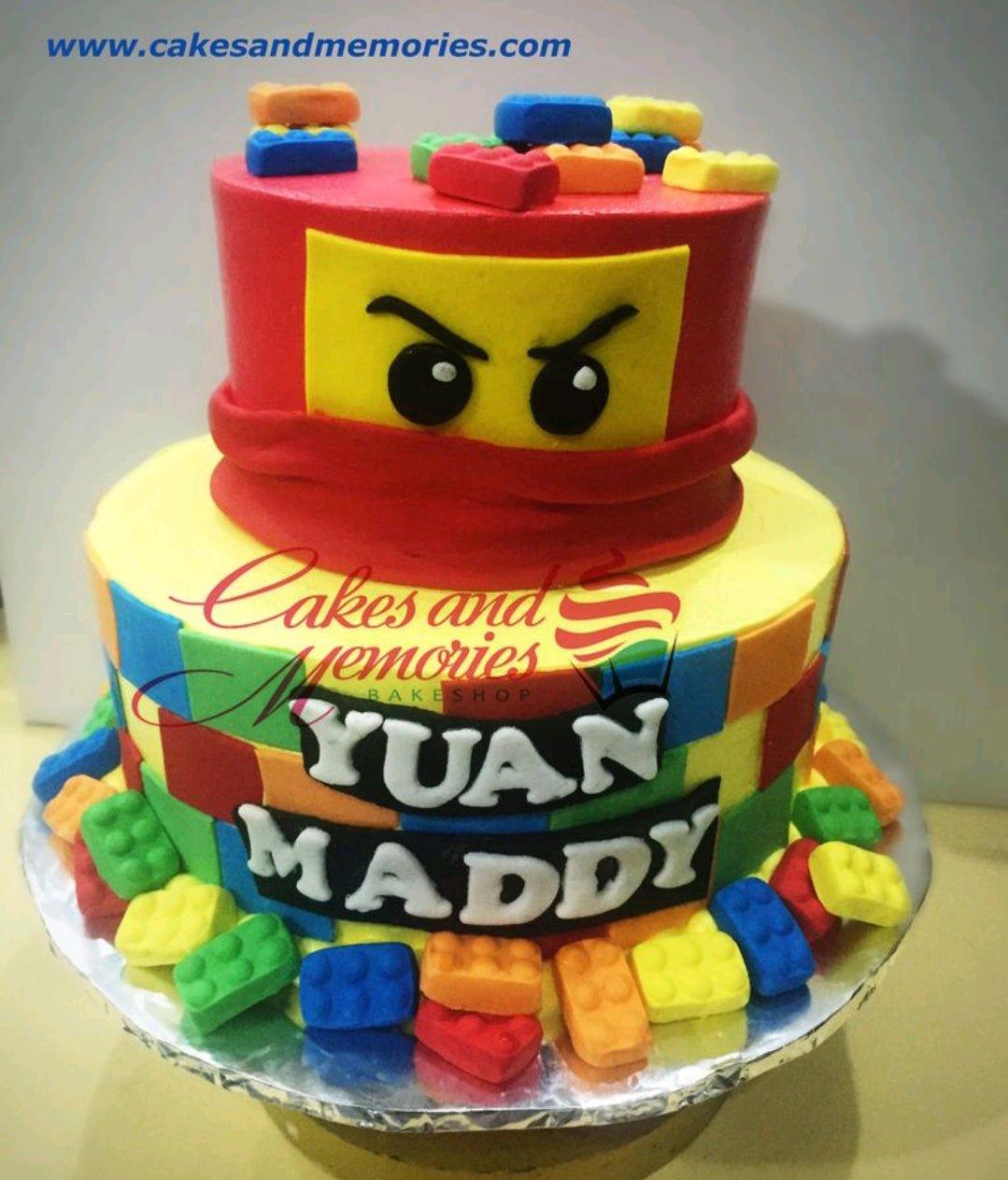 Two-tier Lego Ninjago themed birthday cake with red and yellow fondant, edible Lego bricks, and Ninjago eyes.