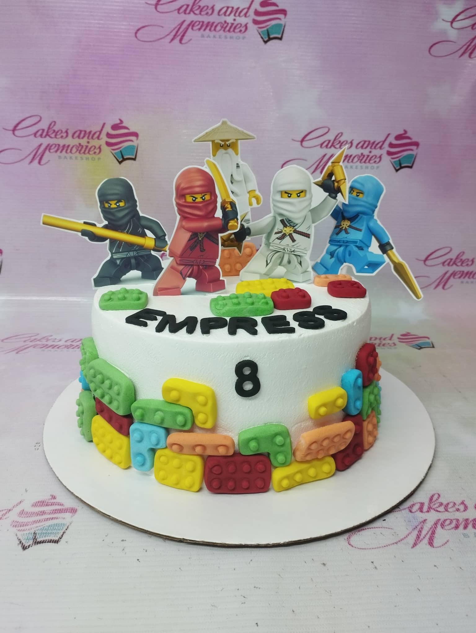 White Lego Ninjago birthday cake with colorful fondant building blocks and character printouts for Empress's 8th birthday.