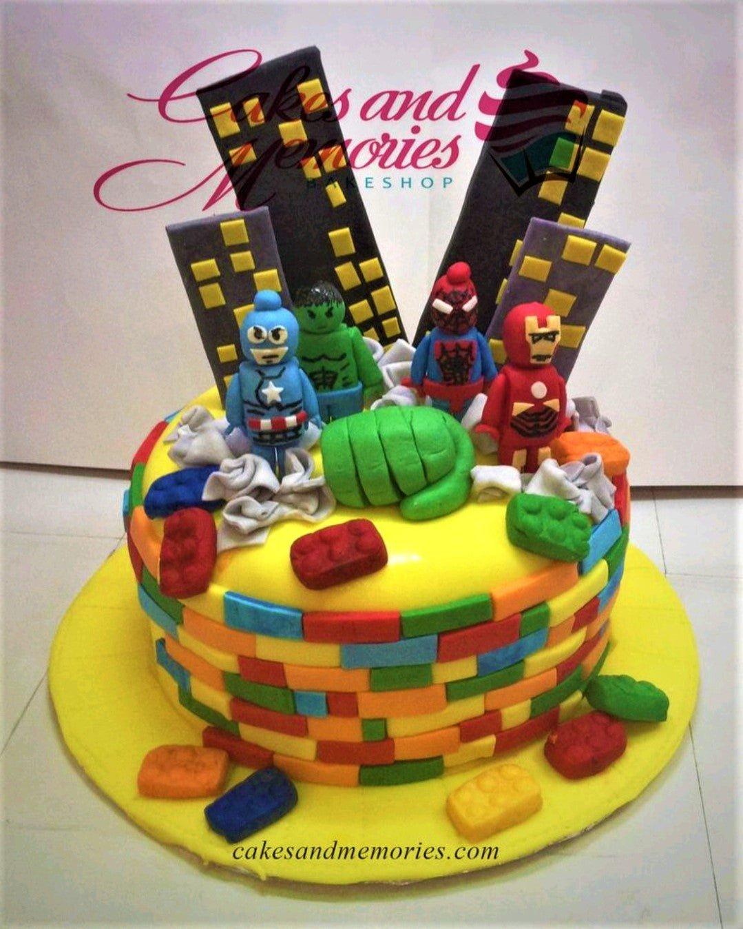Lego-themed superhero cake with fondant figures of Captain America, Hulk, Spider-Man, and Iron Man on a yellow base with edible brick patterns.