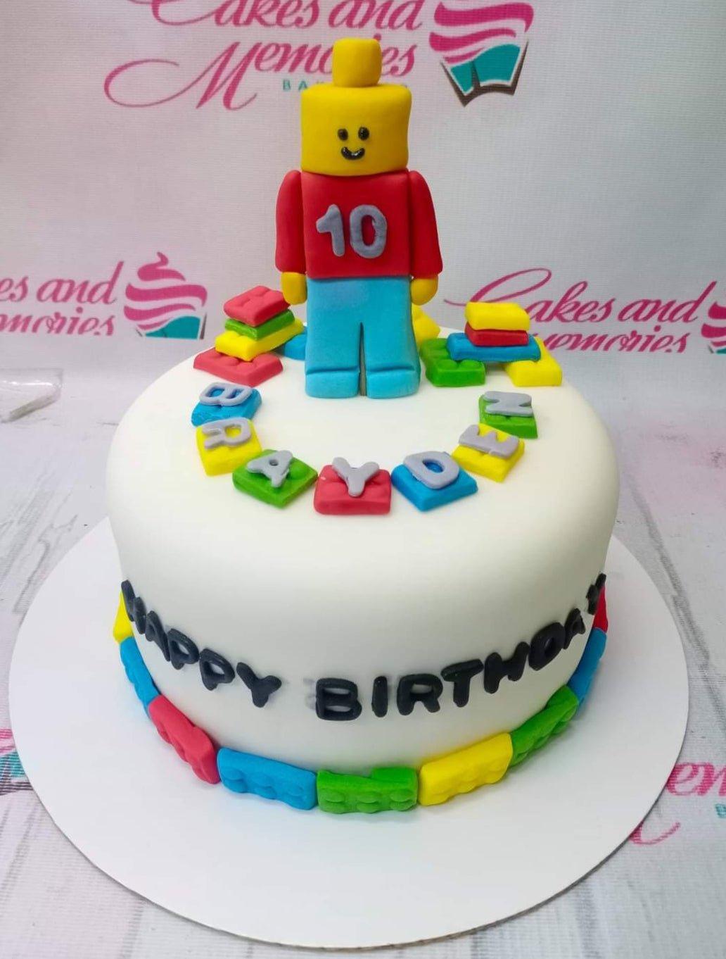 Lego themed birthday cake with a large fondant Lego man topper and colorful Lego brick decorations.