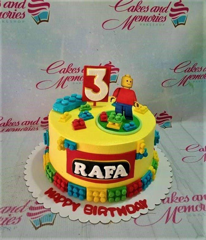 Yellow Lego themed birthday cake with a 3D fondant Lego man, colorful Lego bricks, and a red number 3 topper.
