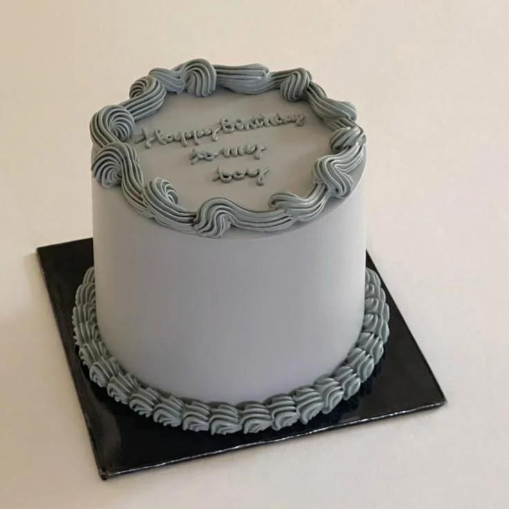 Minimalist light blue birthday cake with piped icing borders and a handwritten message on top.
