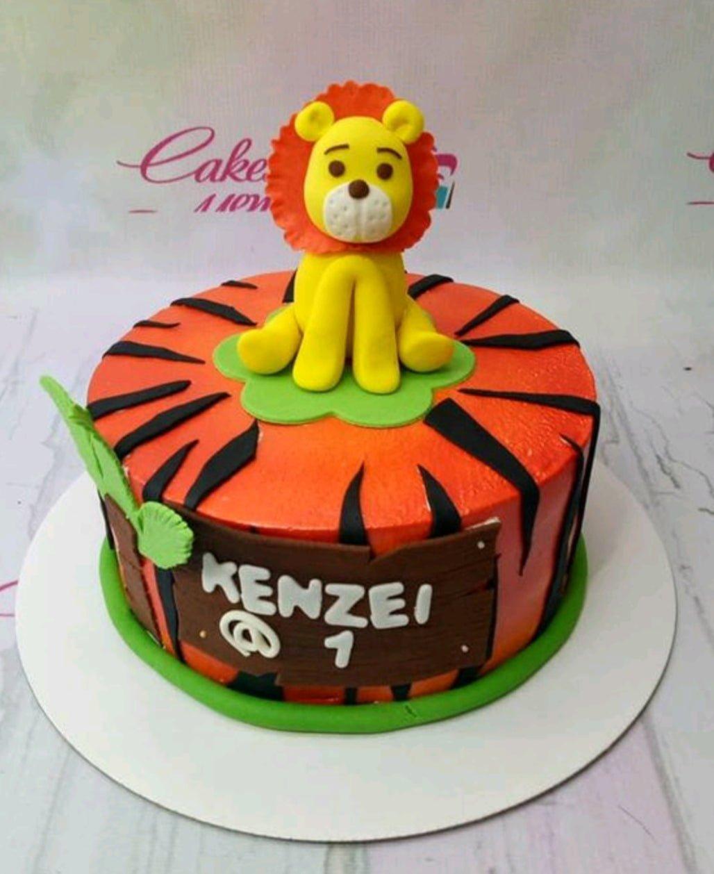 Orange tiger-striped cake with a 3D fondant lion topper and a wooden-style name plaque for Kenzei's 1st birthday.