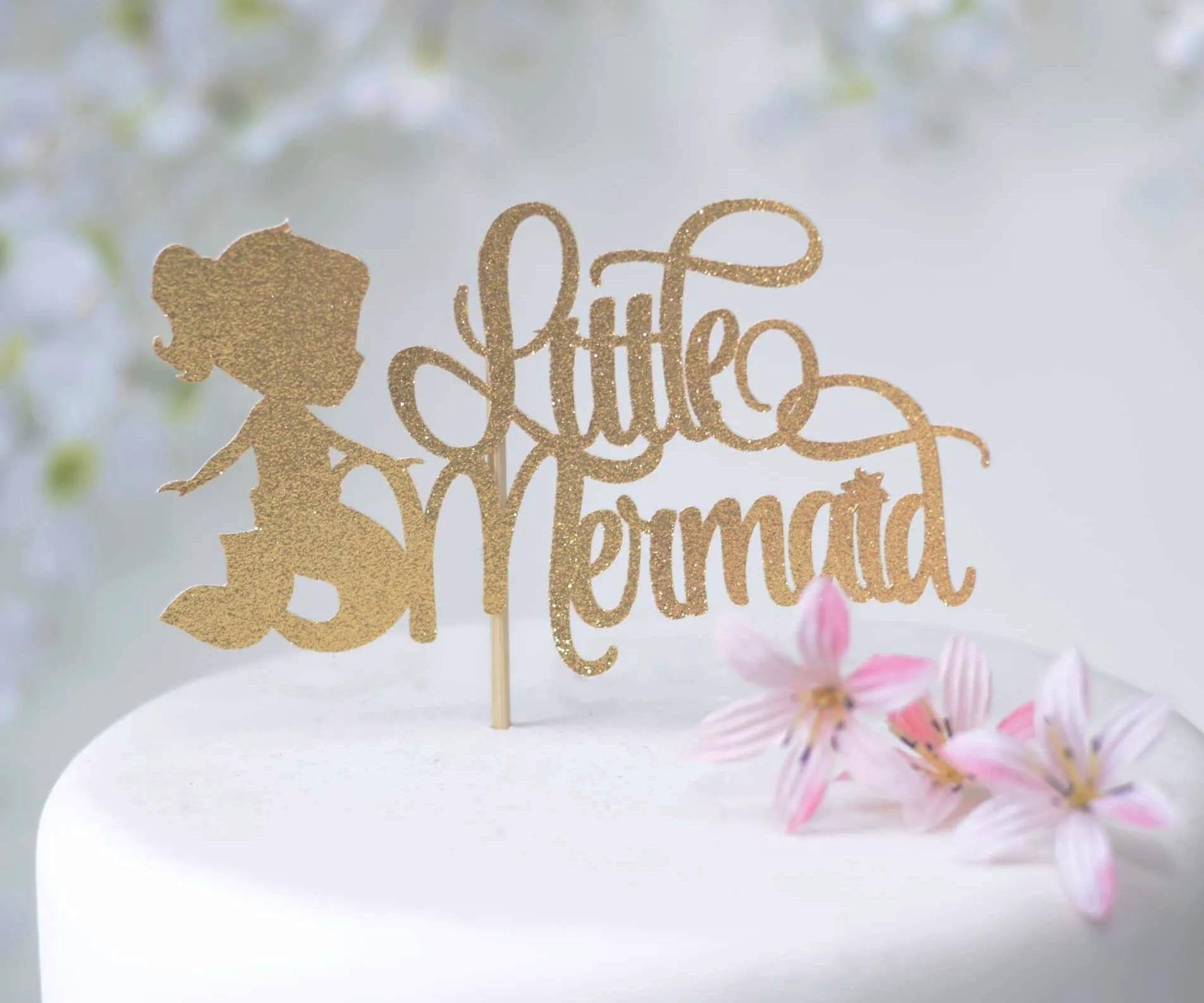 White fondant cake with a gold glitter Little Mermaid topper and pink flowers.