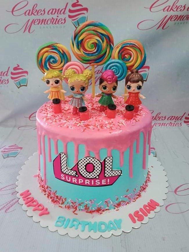 Light blue LOL Surprise themed cake with pink drip, colorful lollipops, and character figurines.