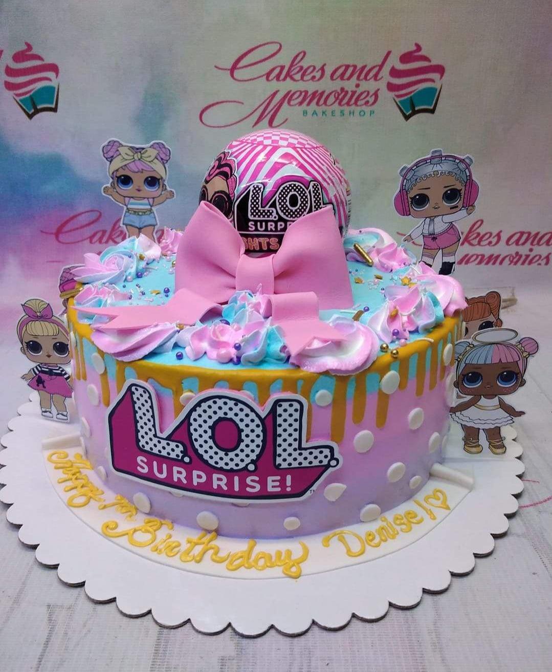 LOL Surprise themed pink and blue birthday cake with character printouts, a large pink bow, and gold drip icing.