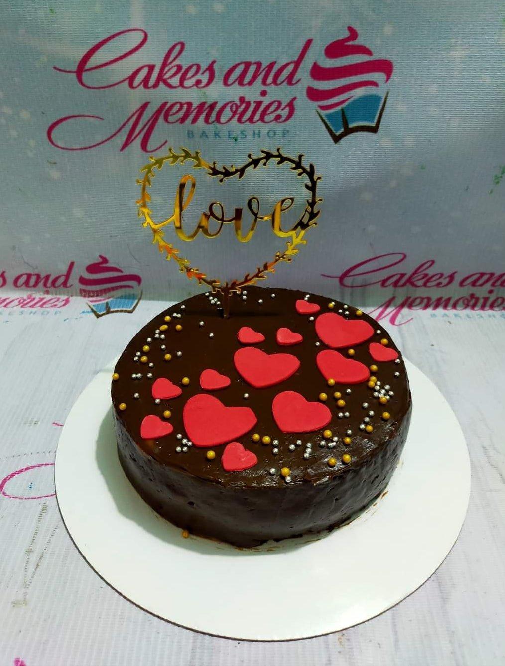 Chocolate cake with red fondant hearts and gold and silver sprinkles, topped with a gold Love heart topper.