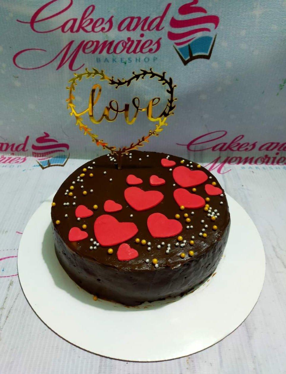 Chocolate cake with red fondant hearts and gold and silver sprinkles, topped with a gold 'love' heart topper.