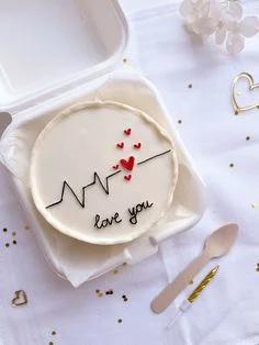 White bento cake with a black heartbeat line, red hearts, and 'love you' message in a takeout container.
