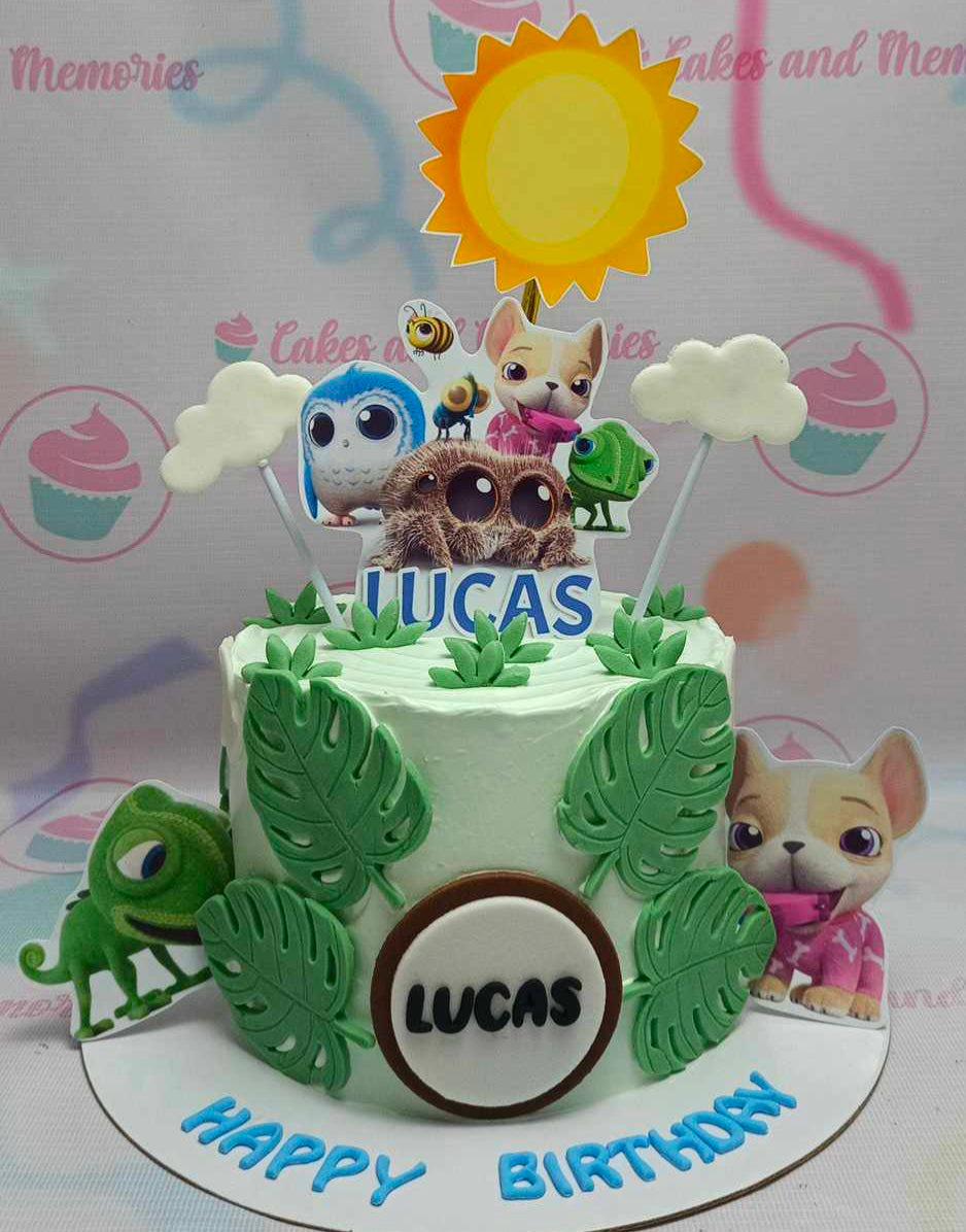 Light green birthday cake with tropical leaves and cartoon animal printouts including a spider, owl, dog, and chameleon.