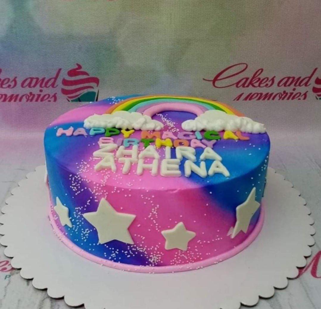 Magical galaxy themed birthday cake with a rainbow topper, white stars, and white clouds on a pink and blue gradient icing.
