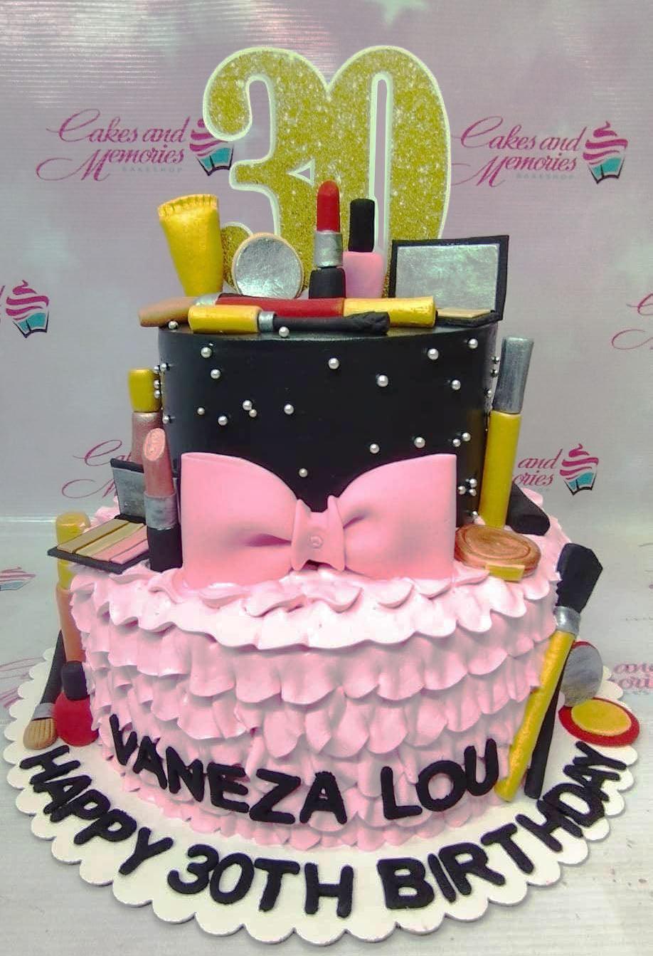 Two-tier makeup themed birthday cake with black fondant top tier, pink ruffled icing bottom tier, and edible 3D makeup toppers.