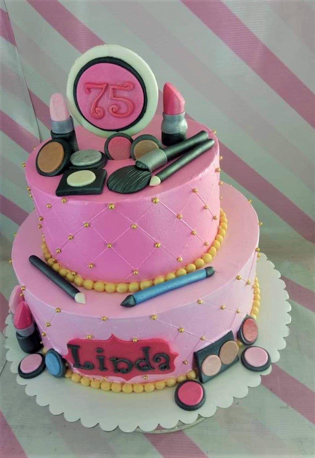 Pink 2-tier makeup themed birthday cake with fondant lipstick, eyeshadow, and brushes for a 75th birthday celebration.