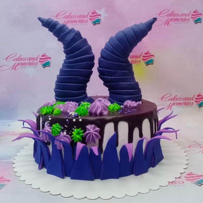 Maleficent themed cake with large purple horns, green and purple icing dollops, and dark chocolate drip on a white base.