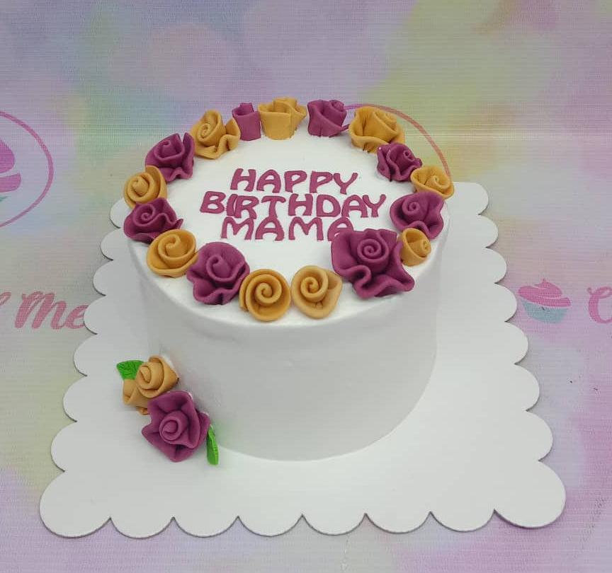 White minimalist birthday cake for Mama featuring a ring of purple and gold fondant roses with a purple icing message.