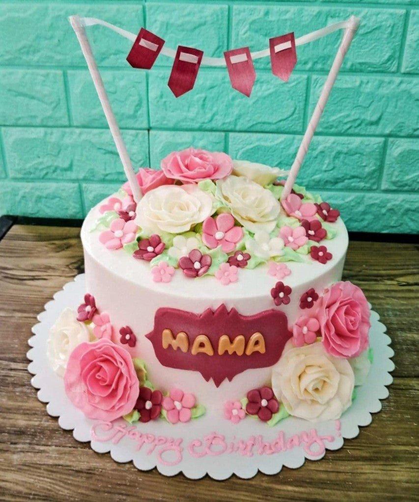 White round cake decorated with pink and white icing roses and a red banner topper for Mama.