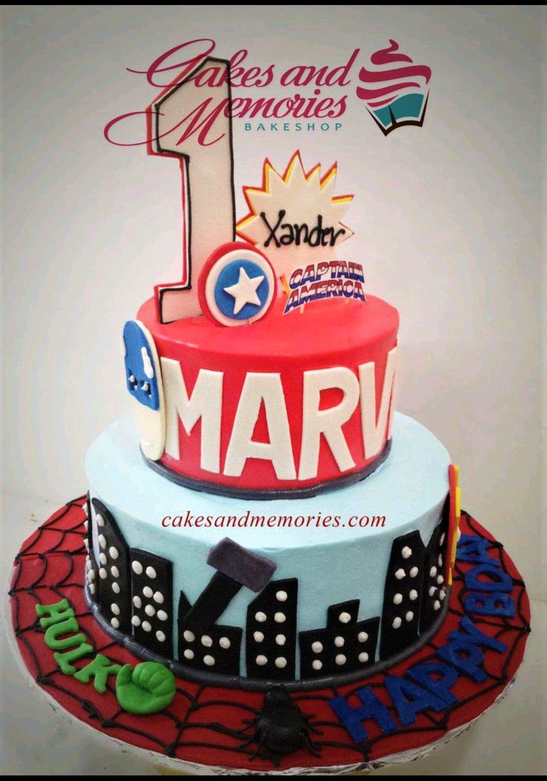Two-tier Marvel Avengers themed birthday cake with Captain America, Thor, Hulk, and Spider-Man elements on a red and light blue fondant base.
