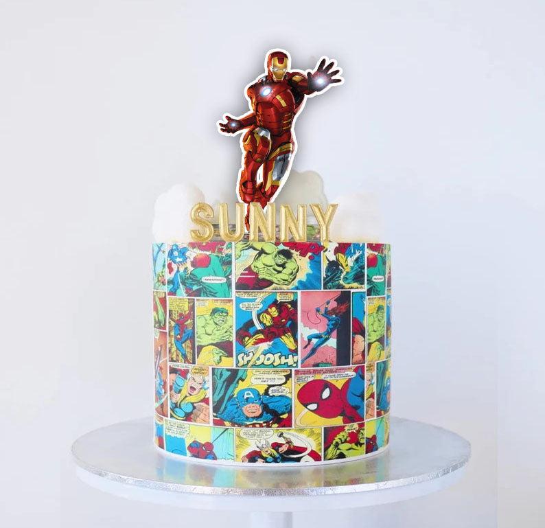 Marvel Avengers comic book themed cake with a large Iron Man printout topper and gold Sunny name topper on white icing clouds.