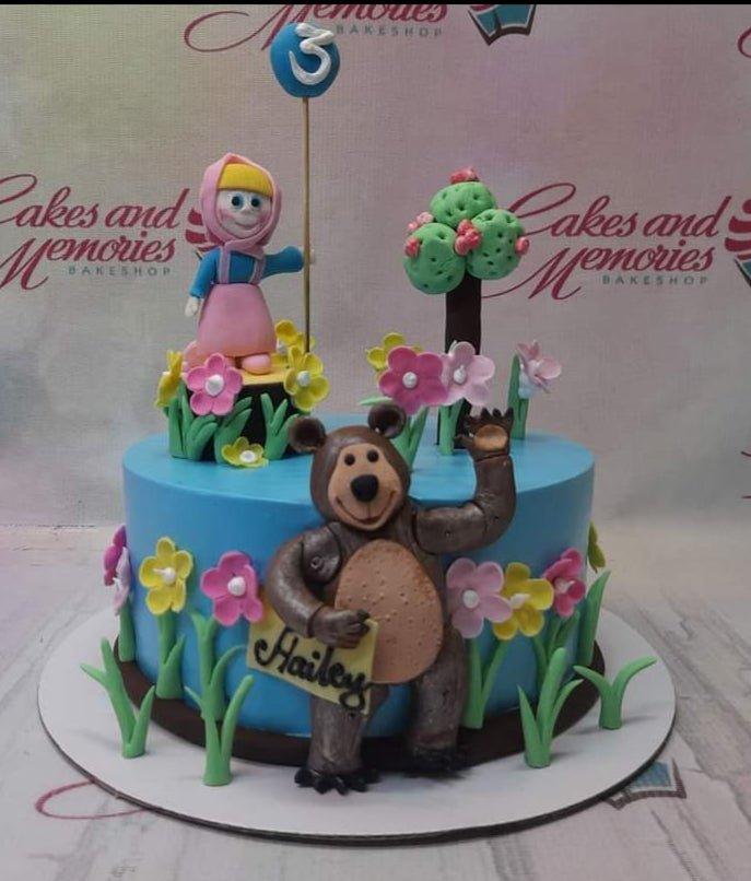 Masha and the Bear themed blue birthday cake with 3D fondant figures of Masha and Bear surrounded by colorful flowers.