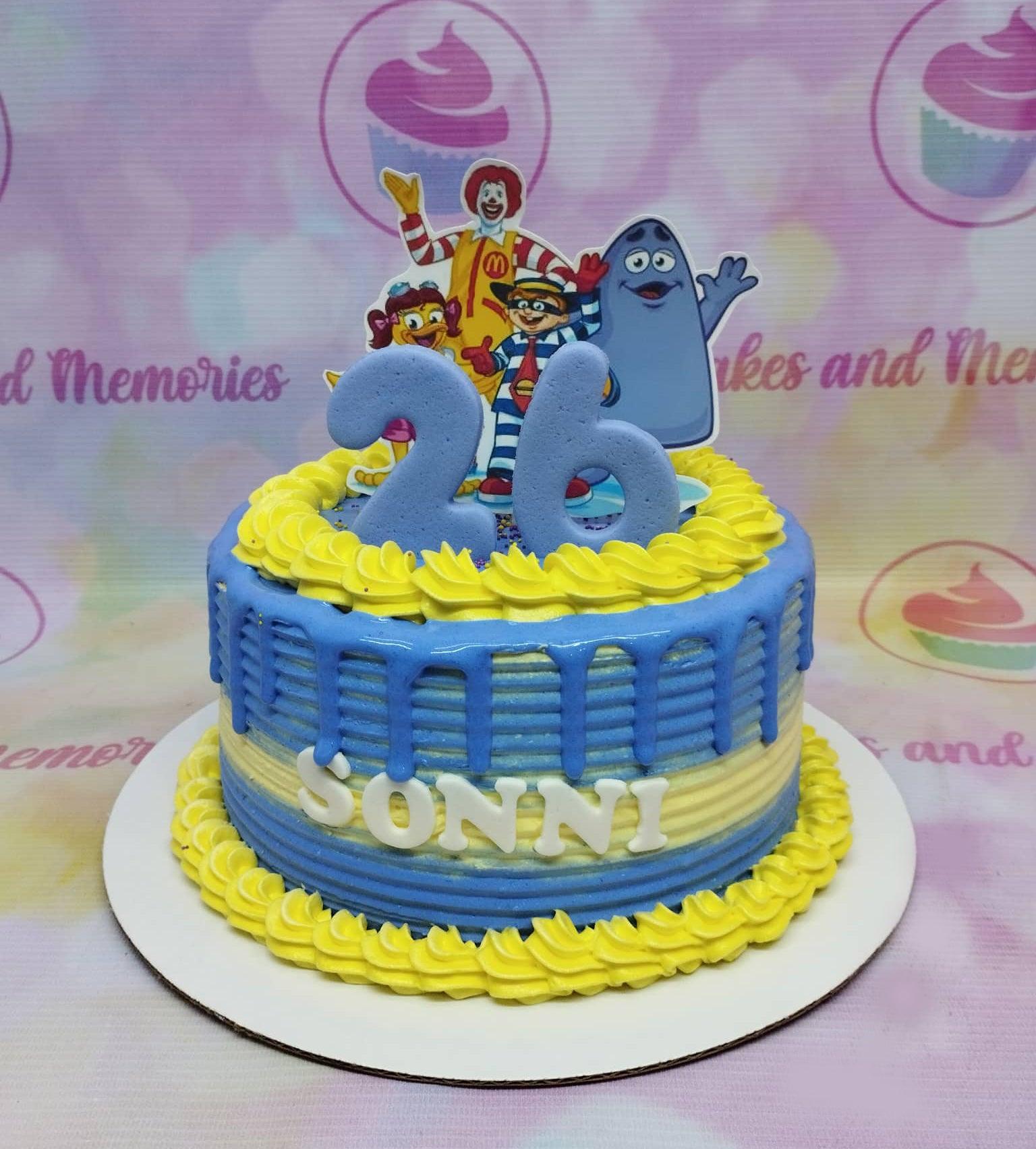 Blue and yellow McDonald's themed birthday cake with Ronald McDonald characters and a large blue number 26 topper.