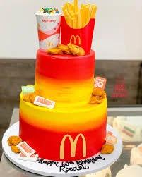 Two-tier McDonald's themed cake with red and yellow gradient icing, featuring 3D fondant nuggets, fries, and a McFlurry cup.